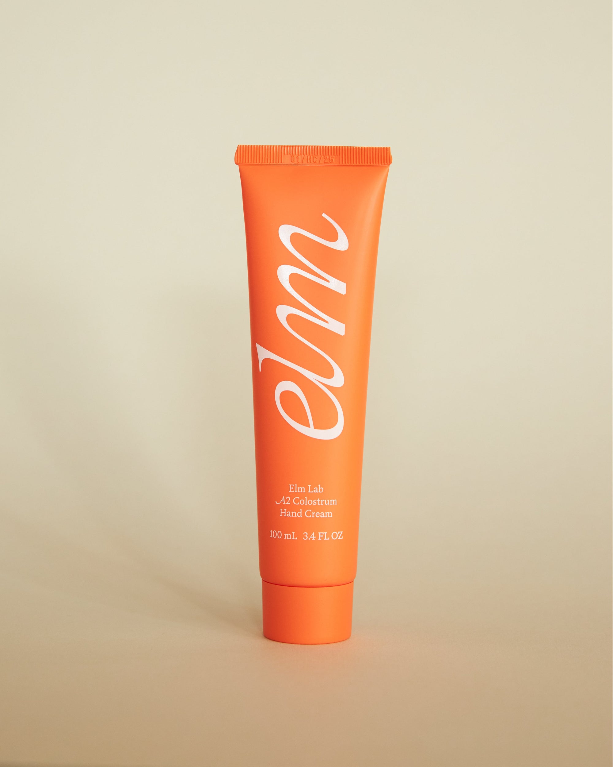 Orange tube of elm hand cream on a beige background