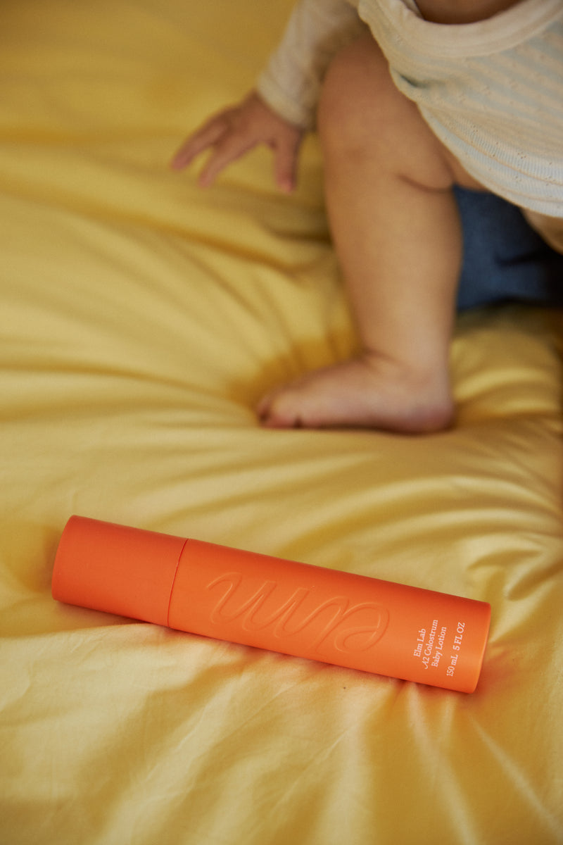 Orange baby lotion on a bed with a child's legs in the background